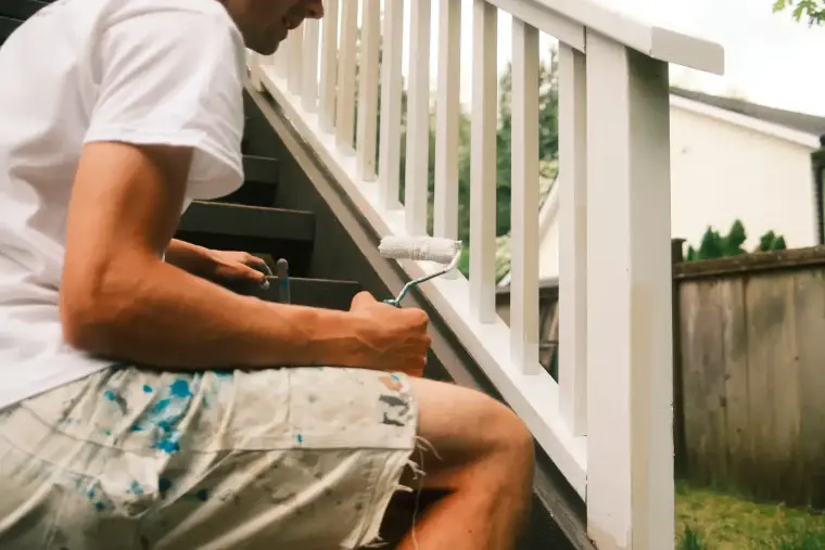 Painter rolling a white baluster railing, deck railing painting by Colour Craft Painting